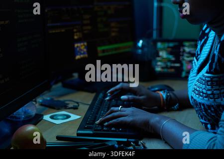 Young Indian Woman Typing Code on Computer Keyboard in Dark Office Stock Photo