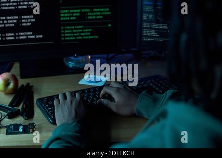 Young Black Man Typing Code on Computer Keyboard in Dark Room Stock Photo