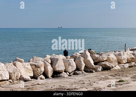 Rear view of senior retired man sitting at seaside looking at horizon over water enjoying freedom, vacation or retirement concept Stock Photo