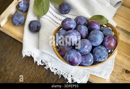 On the table on a napkin wicker basket filled with ripe large plums Stock Photo
