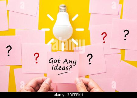 Light bulb shining above pink sticky notes with question marks and text Stock Photo