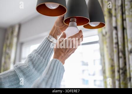Senior woman's hands installing eco light bulb in her home Stock Photo