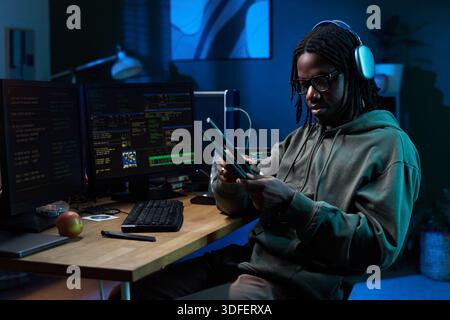 Young Black Man Wearing Headphones Using Tablet at Computer Desk Stock Photo