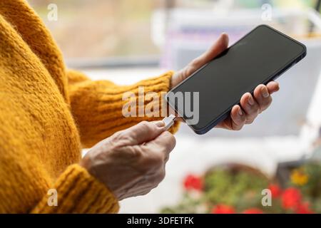 Senior woman connecting USB cable to her cell phone Stock Photo