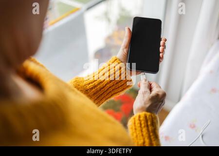Senior woman connecting USB cable to her cell phone Stock Photo