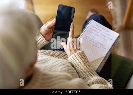 Senior woman using written notes and mobile phone Stock Photo