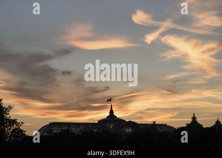View of the Grand Palais silhouette against the vibrant sunset sky, with orange and blue hues blending in harmony, Paris, Île-de-France, France. Stock Photo