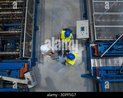 Female manager supervises production while male workers collaborate in a diverse manufacturing setting focused on disability inclusion and teamwork. Stock Photo