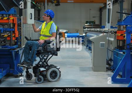 A worker with a disability uses a wheelchair to control an industrial machine in a modern manufacturing environment. Stock Photo