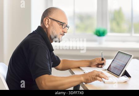 Mature man working with spreadsheet on tablet and calculator at home office Stock Photo