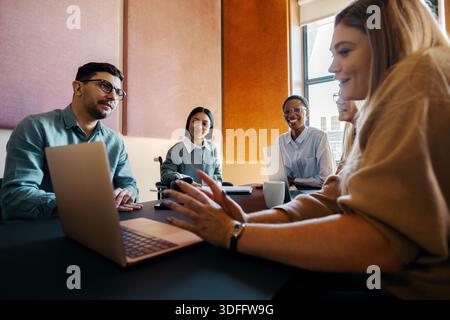 A group of professionals collaborating in a modern meeting room with laptops and documents, fostering teamwork and productivity in a vibrant and diver Stock Photo