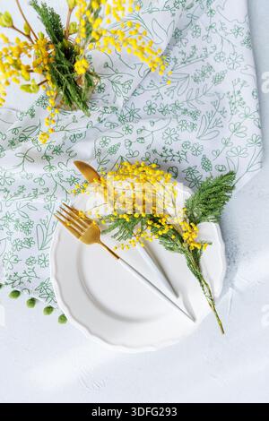 Elegant spring table decor with floral napkin and mimosa flowers Stock Photo