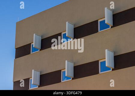 Modern Apartment Building Facade With Shutters, Windows, And Bright Blue Sky Stock Photo