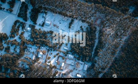 Aerial view of Nowy Lubiel, Poland, snow covers roofs and roads in a loose grid among pine stands. Long tree shadows suggest low sun, cabins and fores Stock Photo