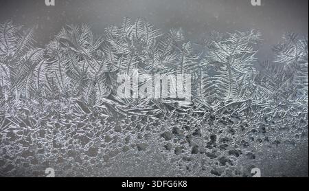 Delicate frost crystals forming fern-like patterns on frozen window. Natural winter texture with ice, condensation and cold atmosphere, ideal for back Stock Photo