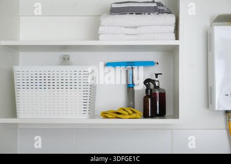 Laundry area featuring stacked towels and cleaning products stored neatly on white shelves Stock Photo