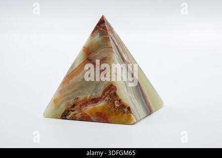 Polished geometric pyramid stone piece displaying layered natural patterns in soft green, beige, and orange tones on a clean white background closeup. Stock Photo