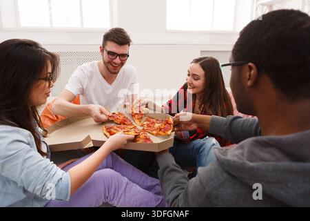 Students sharing pizza at home party Stock Photo