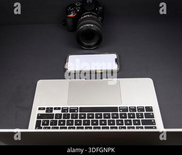 Minimal dark workspace with laptop edge, smartphone blank screen and DSLR camera. Modern content creation setup with copy space. Stock Photo
