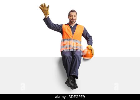 Smiling construction worker sitting on a panel and waving isolated on white background Stock Photo