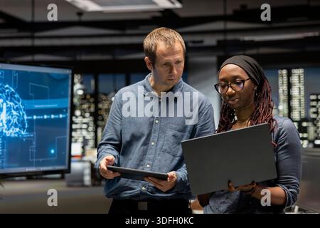 Manager and intern in office automating repetitive tasks using AI scripts on devices. Team leader and trainee work together using artificial intelligence to speed up feature implementation Stock Photo