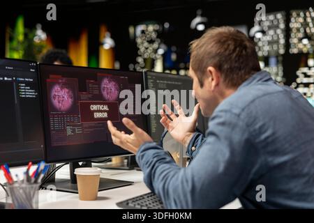 Engineer at office desk frustrated by critical error warning displayed on computer screen. Upset sech startup IT professional annoyed by computer bug affecting server network Stock Photo