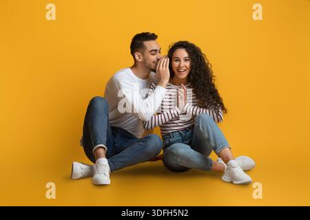 Cheerful Arab Couple Sharing Secrets, Young Man Whispering To His Girlfriend's Ear Stock Photo