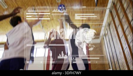 Jumping three players wearing sleeveless jerseys reaching blue-and-white ball in gym, HUD overlay Stock Photo