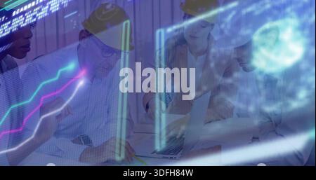 Reviewing team of four wearing hard hats leaning over table at office, viewing laptop, plans Stock Photo