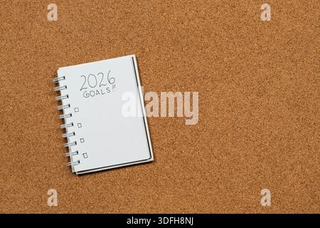 Close up to a white notebook at the left side of the screen with 2026 year goals in blanked over a cork background Stock Photo