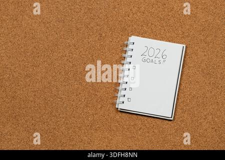 Close up to a white notebook at the right side of the screen with 2026 year goals in blanked over a cork background Stock Photo