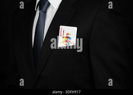 Close up to a businessman on suit with a joker card into his chest pocket with a black background Stock Photo