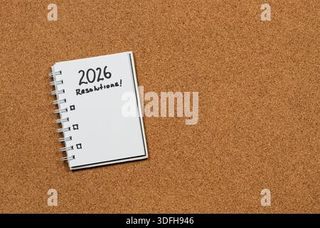 Close up to a white notebook at the left side of the screen with 2026 year resolutions in blanked over a cork background Stock Photo