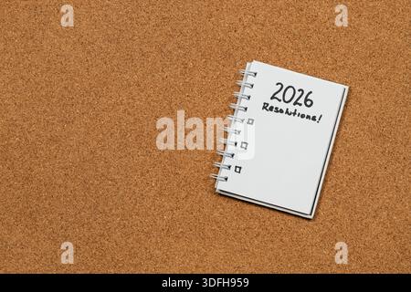 Close up to a white notebook at the right side of the screen with 2026 year resolutions in blanked over a cork background Stock Photo