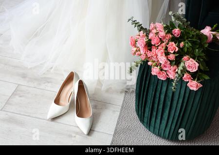 Wedding dress with high heels and roses on pouf in room Stock Photo