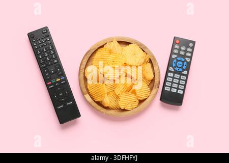 Different modern TV remote controls and board with potato chips on pink background Stock Photo