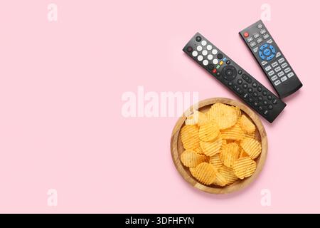 Different modern TV remote controls and board with potato chips on pink background Stock Photo