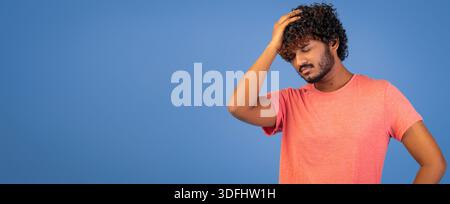 Man With Curly Hair Holds His Head While Standing Against a Blue Background Stock Photo
