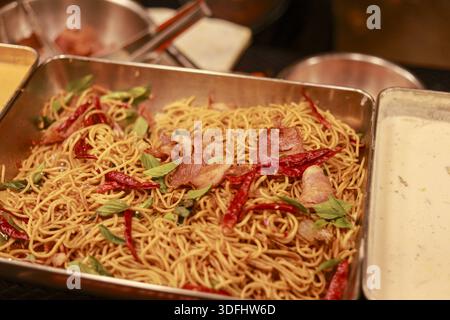 Delicious spicy spaghetti stir fry with dried chili and bacon on stainless tray for buffet catering lunch full of tasty flavor and aromatic smell Stock Photo
