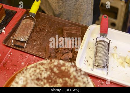 Close up view showing process of preparing delicious sweet dessert with professional metal grater and fresh ingredient like dark chocolate block on me Stock Photo