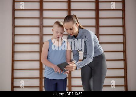 Woman Assisting Child with Down Syndrome Using Digital Tablet Indoors Stock Photo