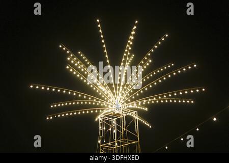 Beautiful glowing starburst light installation shining brightly against dark night sky creating magical festival atmosphere full of joy and holiday ce Stock Photo