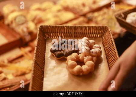 Delicious fresh donut rings with sweet glaze and chocolate topping served on wicker tray in bakery shop for tasty dessert or snack by anonymous hand h Stock Photo