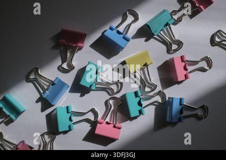 Colorful binder clips scattered on a surface with shadows Stock Photo