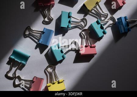 Colorful binder clips scattered on a surface with shadows Stock Photo