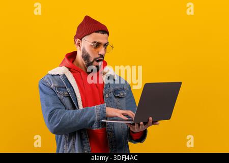 A Man Stands in Front of a Yellow Wall, Wearing a Red Hoodie, Denim Jacket, and a Beanie Stock Photo