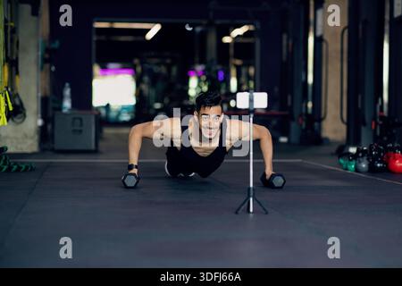 Athletic Arab Man Making Dumbbell Push-Ups While Recording Content On Smartphone Camera Stock Photo