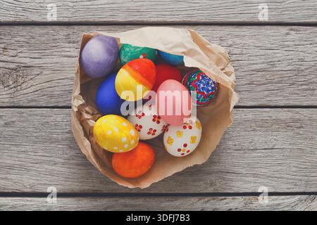 Brightly Colored Easter Eggs Arranged in a Crumpled Paper Bowl on a Wooden Table Stock Photo