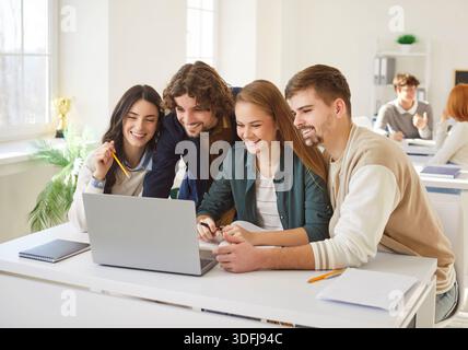 Happy university students collaborating on task, using laptop and preparing project or presentation. Stock Photo