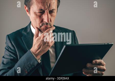 Thoughtful businessman in suit holding tablet with hand on chin, selective focus Stock Photo